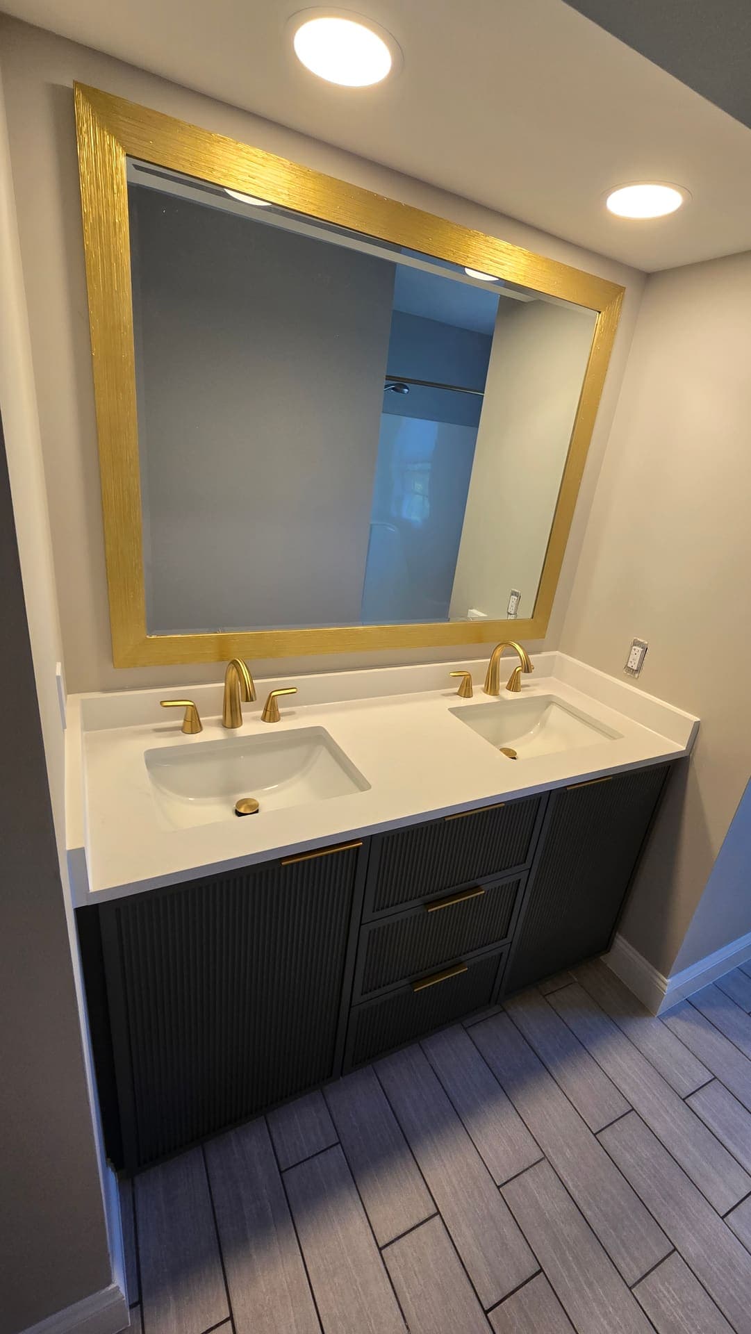 Bathroom with gold framed mirror, gold faucets and black fluted cabinets