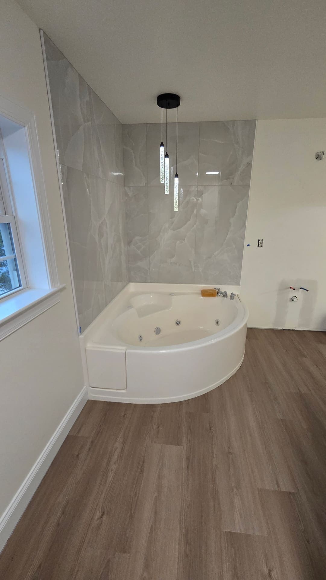 Jetted corner tub with marble tile surround and pendant lighting