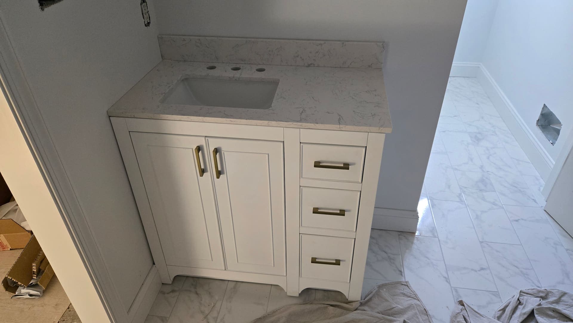 White vanity with brass pulls and marble look floor during install