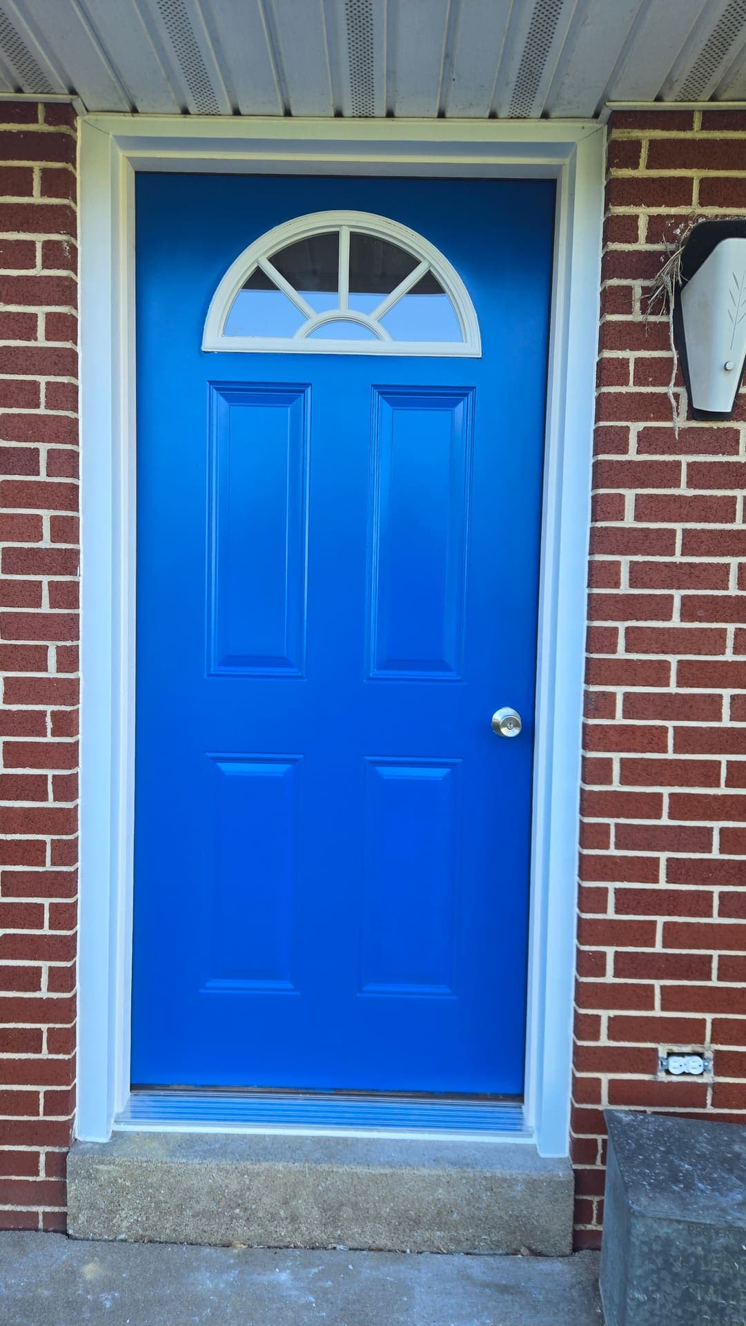 Blue entry door with fan transom on brick and siding
