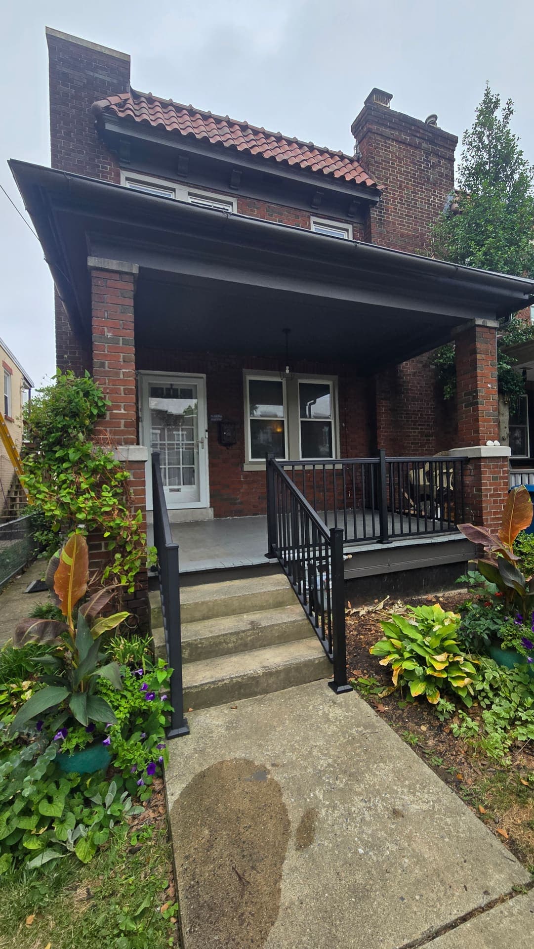 Brick porch with new black metal railings beside a garden